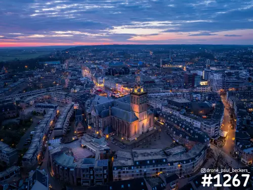 Luchtfoto van de verlichte Stevenskerk in het centrum van Nijmegen na zonsondergang, met roze gloed aan de horizon