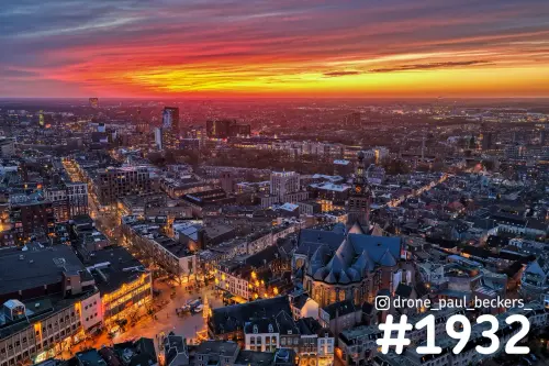 Luchtfoto van het centrum van Nijmegen na zonsondergang, met de verlichte Stevenskerk en een rood-oranje lucht boven de daken