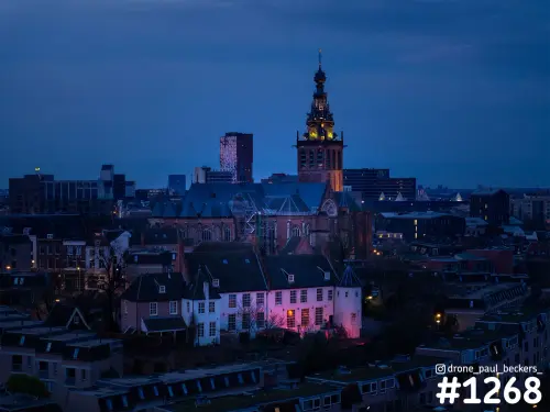 Luchtfoto van de Stevenskerk in het centrum van Nijmegen in het blauwe avonduur, met verlichte toren en roze aangelicht huis