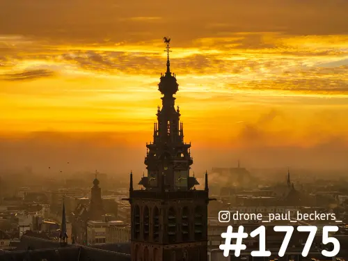 Luchtfoto van de Stevenskerktoren in Nijmegen tegen een goudoranje lucht, met nevel boven de daken van het centrum