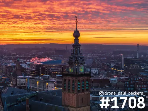 Luchtfoto van de Stevenskerktoren in het centrum van Nijmegen met een oranjerode wolkenlucht en stoom boven de daken