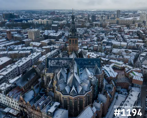 Luchtfoto van de Stevenskerk in het centrum van Nijmegen onder een laag sneeuw, met besneeuwde daken en de toren op de achtergrond