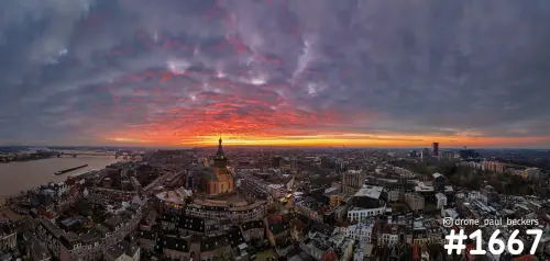 Panoramische luchtfoto van het centrum van Nijmegen met de Stevenskerk onder een felrode zonsondergang en de Waal links