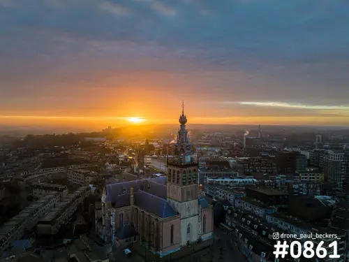 Luchtfoto van de Stevenskerk in het centrum van Nijmegen bij zonsopkomst, met oranje gloed boven de daken