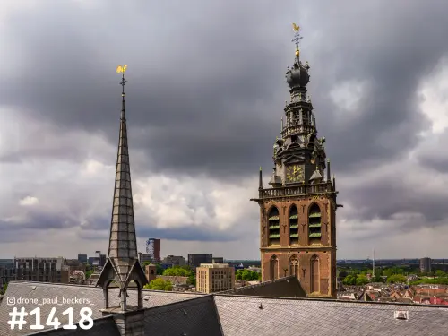 Luchtfoto van de Stevenskerk in Nijmegen met donkere wolken, de klokkentoren en een slanke spits met gouden haan