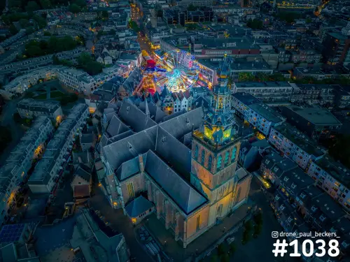 Luchtfoto van de verlichte Stevenskerk in Nijmegen in de avondschemering, met een reuzenrad van de kermis achter de kerk