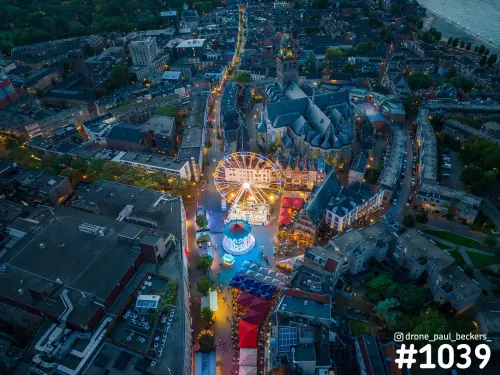 Luchtfoto van de kermis rond de Stevenskerk in Nijmegen in de avondschemering, met verlicht reuzenrad en draaimolen