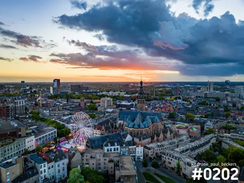 Luchtfoto van de Stevenskerk in Nijmegen in avondlicht, met verlicht reuzenrad van de kermis en donkere regenwolken