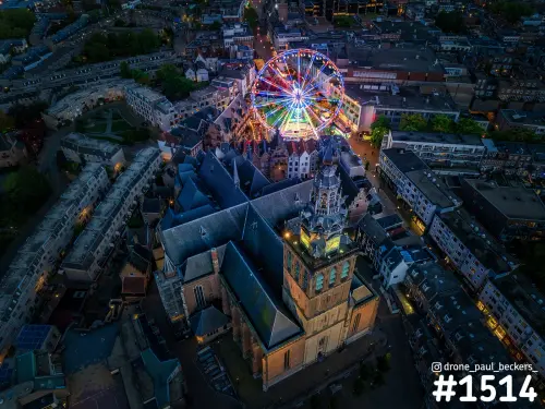 Luchtfoto van de Stevenskerk in Nijmegen in de avondschemering, met het verlichte reuzenrad van de kermis op de Grote Markt