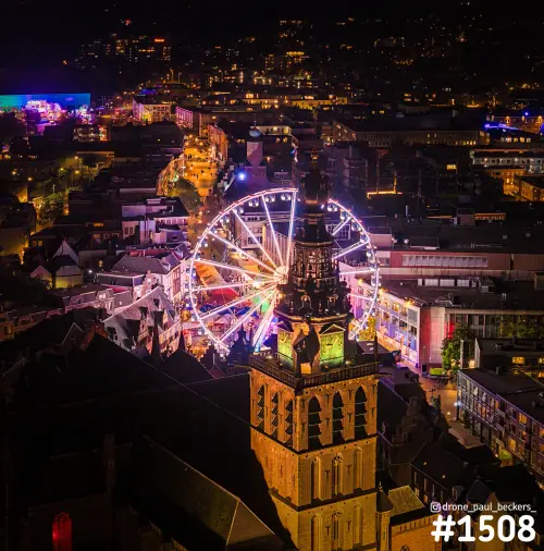 Luchtfoto van de Stevenskerk in Nijmegen bij nacht, met het verlichte reuzenrad van de kermis op de Grote Markt erachter