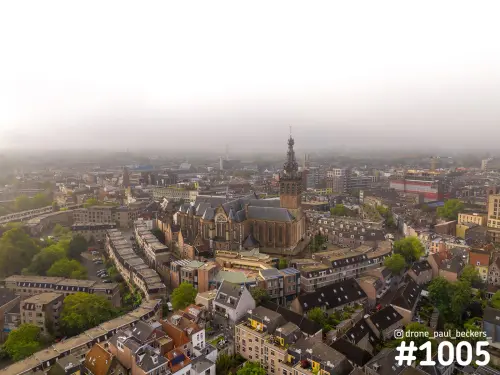 Luchtfoto van de Stevenskerk in Nijmegen in ochtendmist, met daken van de binnenstad en groene bomen op de voorgrond