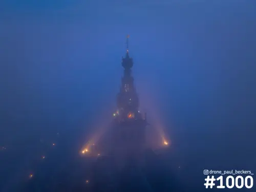 Luchtfoto van de Stevenskerk in Nijmegen in dichte mist in het blauwe uur, met verlichte toren en lichtbundels in de nevel