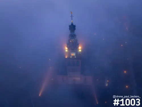 Luchtfoto van de Stevenskerk in Nijmegen in dikke mist, met de verlichte toren die door het blauwe avondlicht prikt