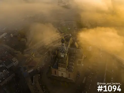 Luchtfoto van de Stevenskerk in Nijmegen met gouden ochtendlicht en mist die tussen de daken van de binnenstad hangt