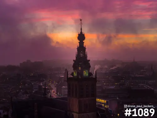 Luchtfoto van de Stevenskerktoren in Nijmegen in mist, met paarse en oranje lucht en verlichte wijzerplaten