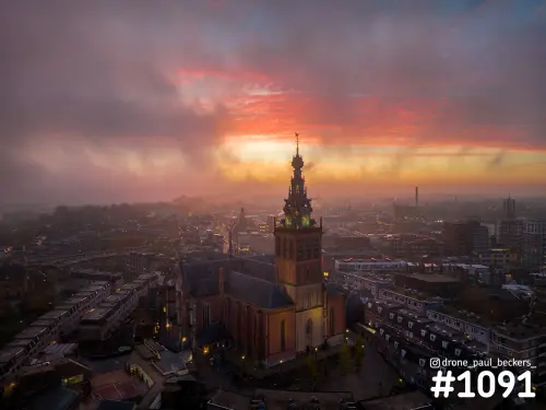 Luchtfoto van de Stevenskerk in Nijmegen onder een rood-oranje lucht, met mist boven de daken van de stad