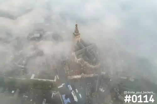 Luchtfoto van de Stevenskerk in Nijmegen met de toren boven de laag mist uit, omringd door daken en pleinen
