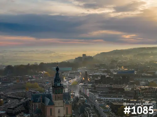 Luchtfoto van de Stevenskerk in Nijmegen bij zonsopkomst, met mist boven het landschap achter de daken van de stad