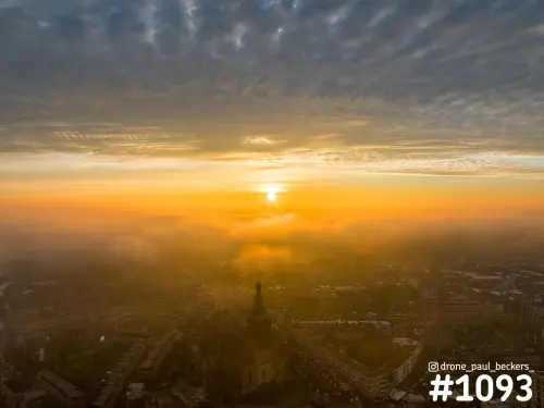Luchtfoto van de Stevenskerk in Nijmegen met laagstaande oranje zon boven de mist en een golvend wolkendek boven de daken
