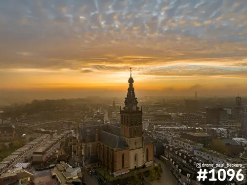 Luchtfoto van de Stevenskerk in Nijmegen bij zonsopkomst, met mist boven de daken en een lucht vol schaapjeswolken