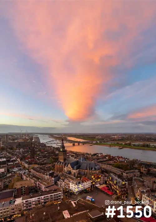 Luchtfoto van de Stevenskerk en de Grote Markt in Nijmegen met een roze wolk boven de Waal in het avondlicht