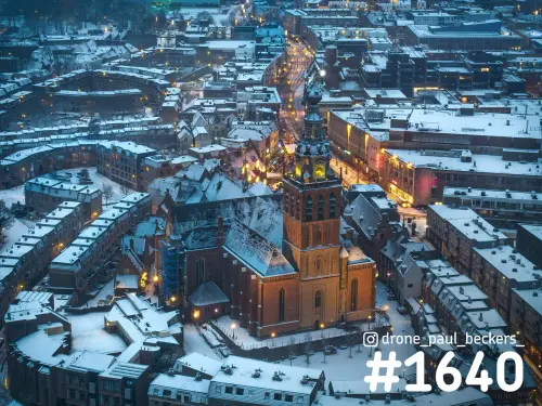 Luchtfoto van de Stevenskerk in het centrum van Nijmegen in de sneeuw, met verlichte straten in de avondschemering