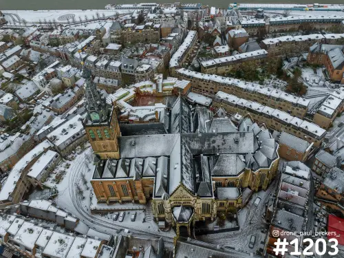 Luchtfoto van de Stevenskerk in Nijmegen met sneeuw op de daken, de toren links en de Waal bovenaan in beeld