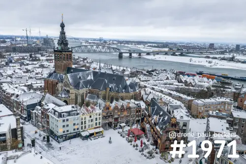 Luchtfoto van de Stevenskerk in Nijmegen onder een laag sneeuw, met de Grote Markt en de brug over de Waal