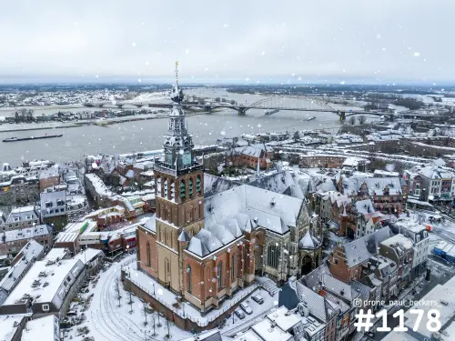 Luchtfoto van de Stevenskerk in Nijmegen onder sneeuwval, met de Waal en de Waalbrug op de achtergrond