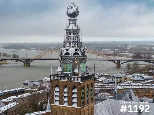 Luchtfoto van de toren van de Stevenskerk in Nijmegen, met sneeuw op de daken en de Waalbrug op de achtergrond