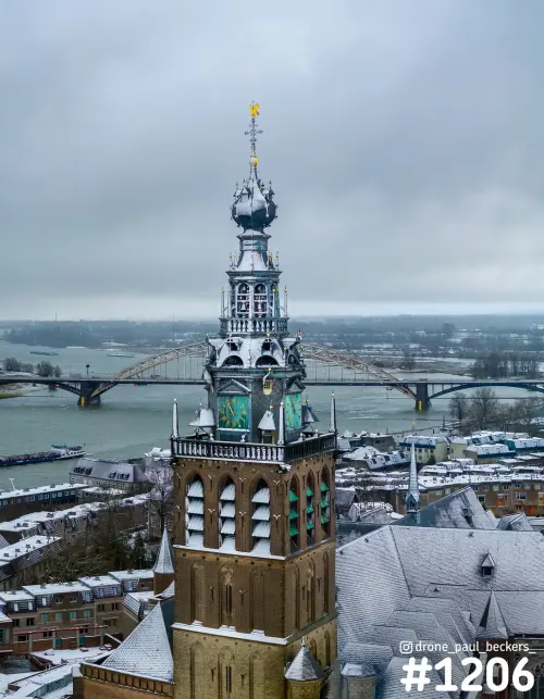 Luchtfoto van de Stevenskerk in Nijmegen met sneeuw op de daken, met de Waalbrug en de rivier de Waal op de achtergrond