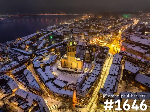 Luchtfoto van de Stevenskerk in Nijmegen in de winteravond, sneeuw op de daken van het centrum en de Waal op de achtergrond