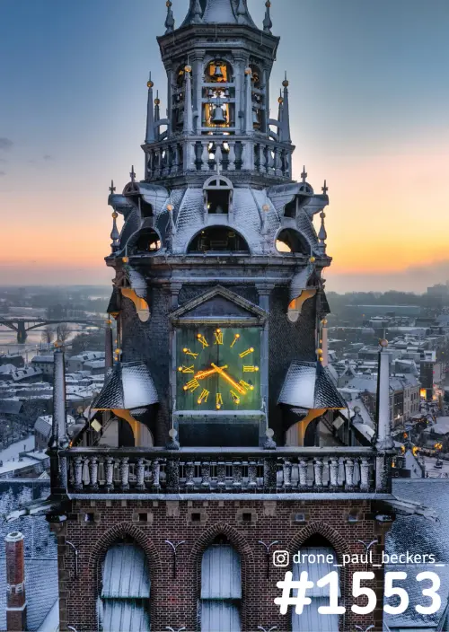 Luchtfoto van de Stevenskerk in Nijmegen met verlichte klokkenwijzer en besneeuwde daken bij zonsondergang