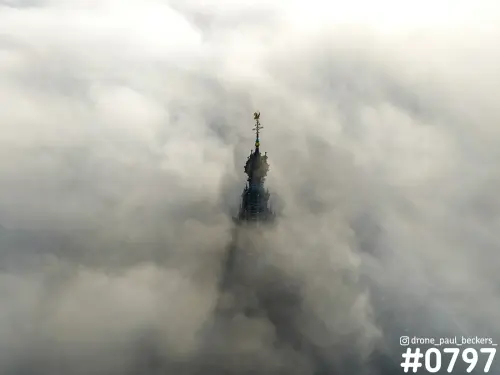 Luchtfoto van de torenspits van de Stevenskerk in Nijmegen, die boven een dik pak mist uitsteekt met gouden windvaan
