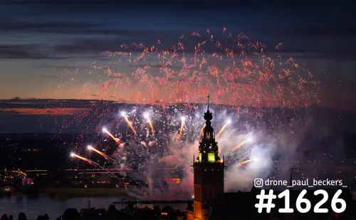 Luchtfoto van vuurwerk boven de Stevenskerk in Nijmegen in de avondschemering, met rookwolken en de rivier op de achtergrond