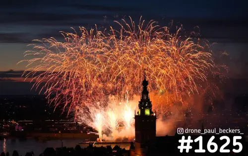 Luchtfoto van vuurwerk boven de Stevenskerk in Nijmegen, met oranje vuurwerkbogen en rookwolken in de avondschemering