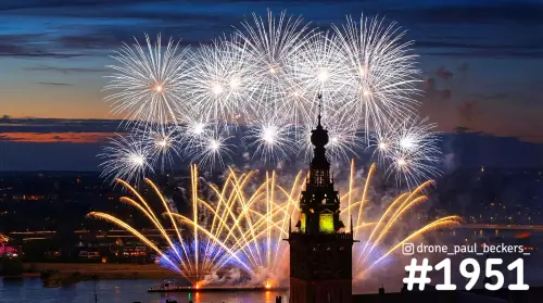 Luchtfoto van vuurwerk boven de Waal in Nijmegen, met de verlichte toren van de Stevenskerk in de avondschemering