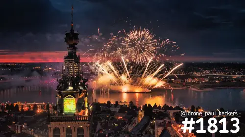 Luchtfoto van vuurwerk boven de Waal in Nijmegen met de verlichte Stevenskerktoren en een rode avondgloed