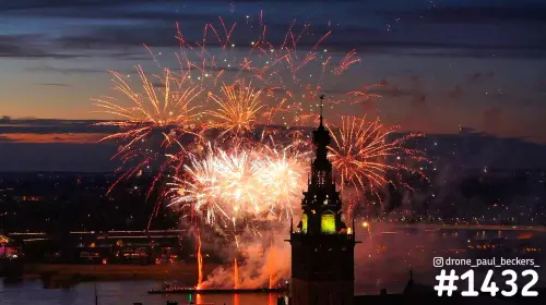 Gouden en witte vuurwerkbollen boven de Waal in Nijmegen, met de groen verlichte toren van de Stevenskerk en rook