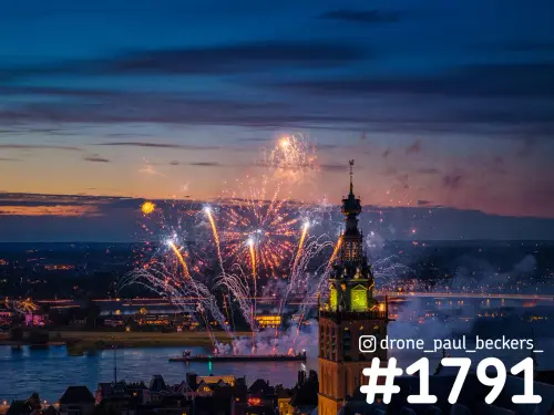 Luchtfoto van vuurwerk boven de Waal in Nijmegen bij schemering, naast de verlichte toren van de Stevenskerk