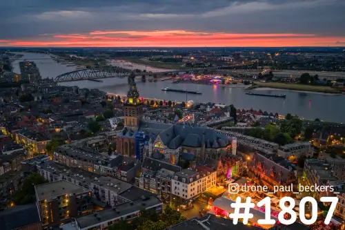 Luchtfoto van de Stevenskerk en de Grote Markt in Nijmegen bij schemering, met de Waal en een rood avondrood aan de horizon
