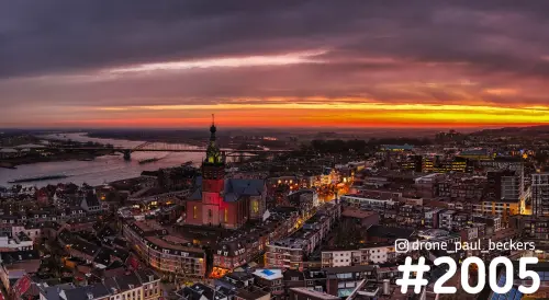 Luchtfoto van de verlichte Stevenskerk in het centrum van Nijmegen in de avondschemering, met de Waal en Waalbrug links