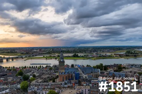 Luchtfoto van de Stevenskerk in Nijmegen met de Waal, Lent aan de overkant en dreigende wolken met oranje gloed
