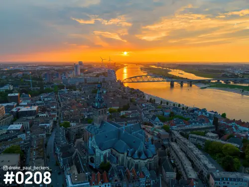 Luchtfoto van de Stevenskerk en het centrum van Nijmegen, met de Waal en een brug in oranje licht van de laagstaande zon