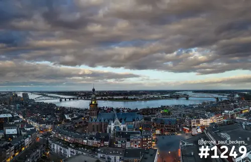 Luchtfoto van de Stevenskerk in Nijmegen in de schemering, met de Waal en bruggen onder een zware wolkenlucht