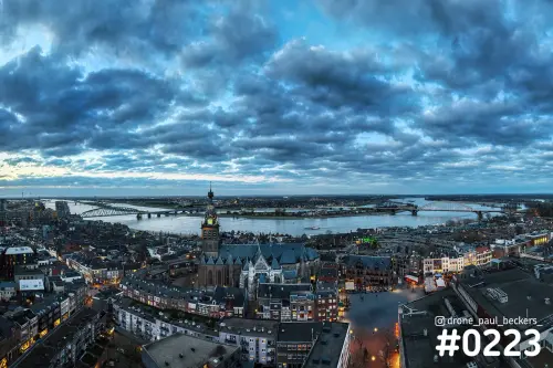 Luchtfoto van de Stevenskerk in Nijmegen in de schemering, met de Waal en de Waalbrug onder een zware wolkenlucht