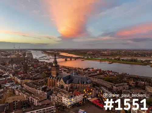 Luchtfoto van de Stevenskerk en de Grote Markt in Nijmegen bij zonsondergang, met de Waal en een oranje wolk