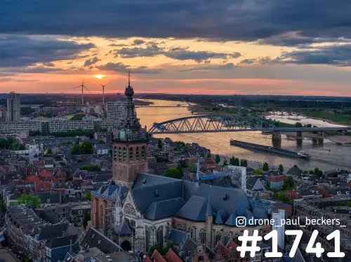 Luchtfoto van de Stevenskerk in Nijmegen bij zonsondergang, met de Waal en een stalen boogbrug achter de daken