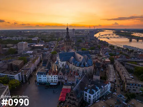 Luchtfoto van de Stevenskerk in Nijmegen bij zonsondergang, met de Waal en een brug aan de horizon