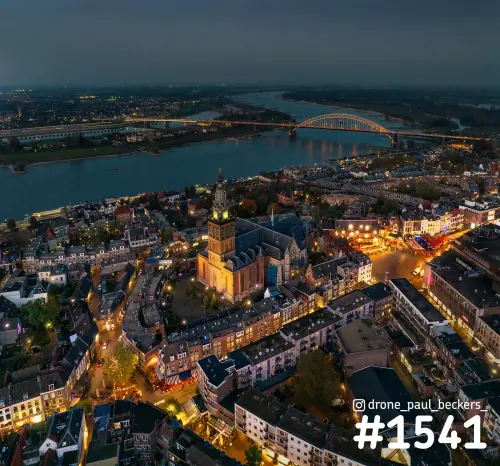 Luchtfoto van de Stevenskerk en de Grote Markt in Nijmegen in het blauwe uur, met de verlichte Waalbrug over de Waal
